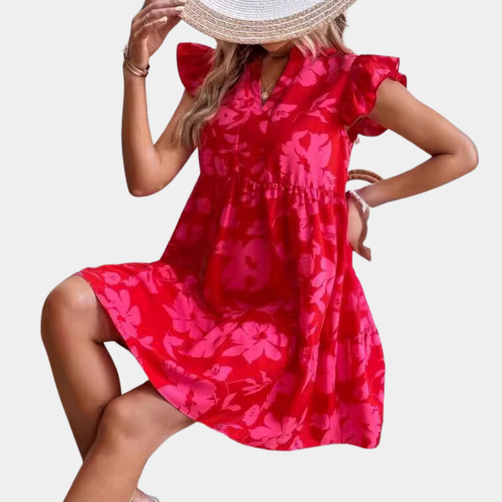 Vrouw in rode zomerjurk met bloemenprint en ruches, zittend met hoed. Trendy damesmode, casual zomeroutfit, stijlvolle jurk.