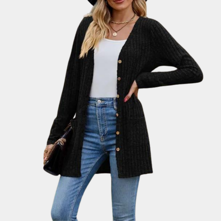 Zwarte damesvest met knopen, lange mouwen en zakken, gedragen over een witte top en blauwe jeans. Perfect voor casual en stijlvolle outfits.