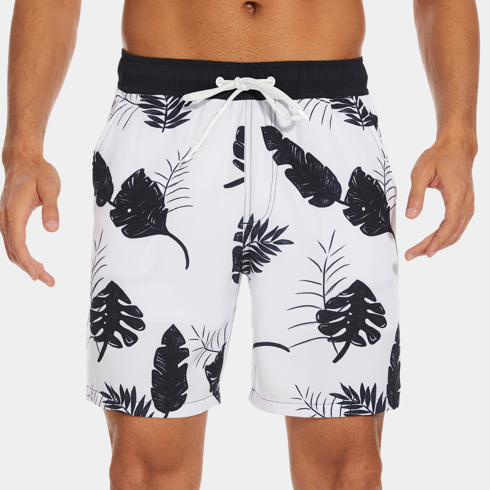 Witte zwembroek met zwarte tropische bladerenprint, elastische tailleband en trekkoord. Perfect voor strandmode en zomerse activiteiten.