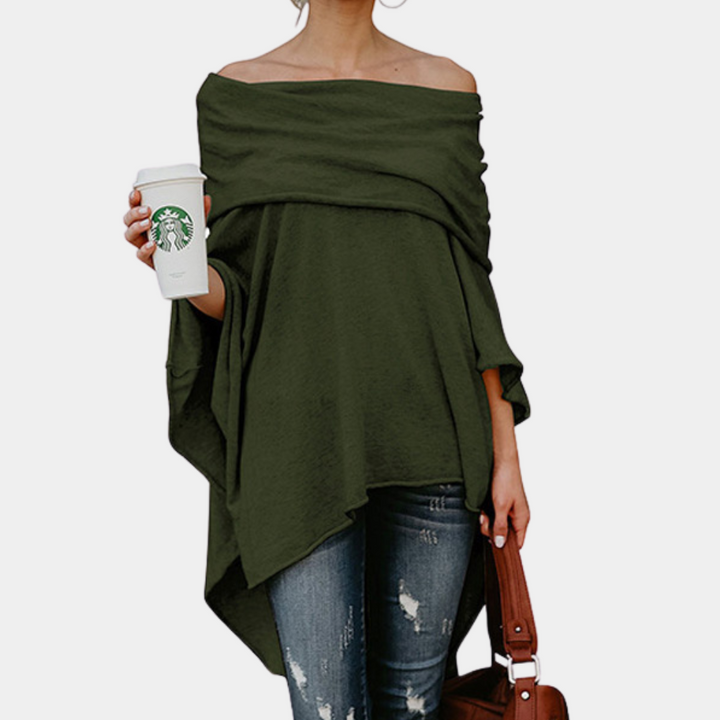 Vrouw in off-shoulder groene poncho, draagt gescheurde jeans en houdt Starbucks-beker en bruine tas vast. Modieuze casual dameskleding.