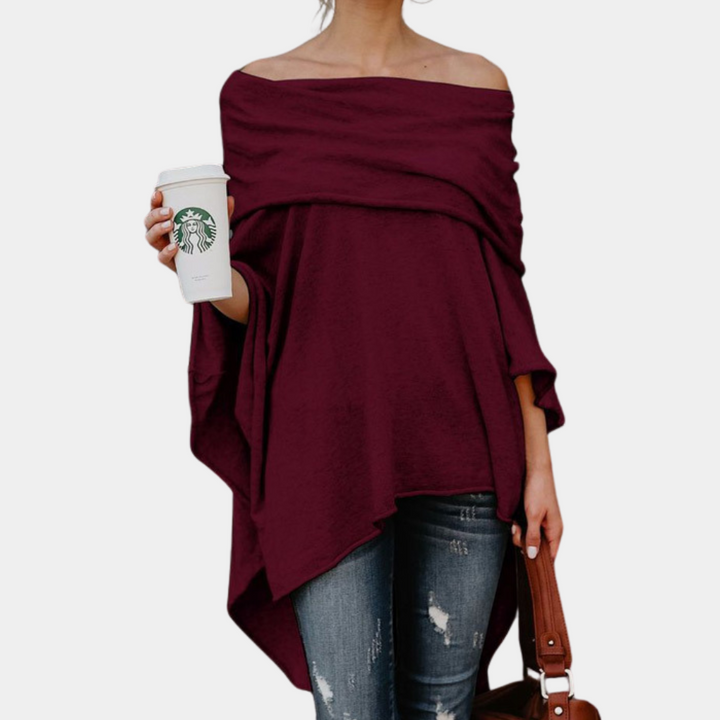 Vrouw in bordeauxrode off-shoulder poncho, draagt een Starbucks-beker en bruine tas, casual outfit, trendy damesmode, herfstkleding.