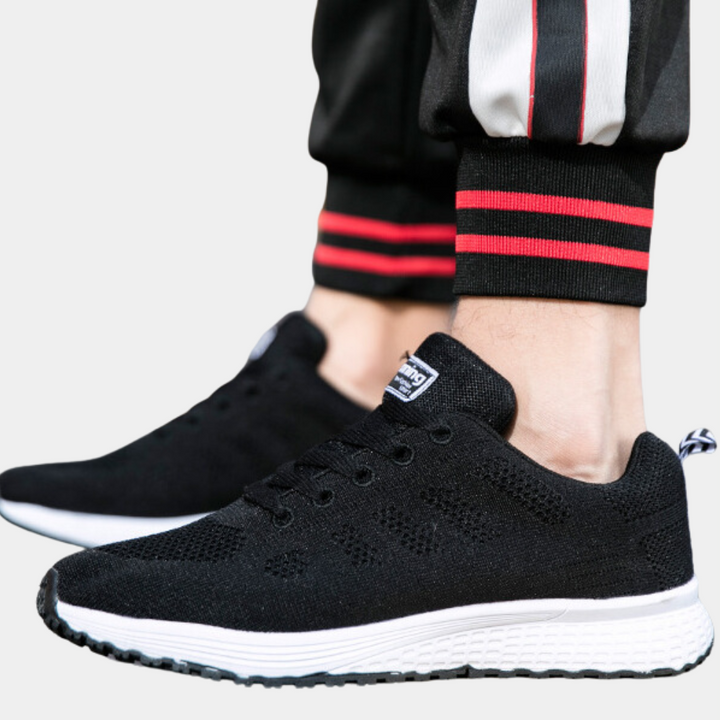Zwarte sportschoenen met witte zool, gedragen door persoon in sportbroek met rode strepen. Comfortabele hardloopschoenen voor heren.