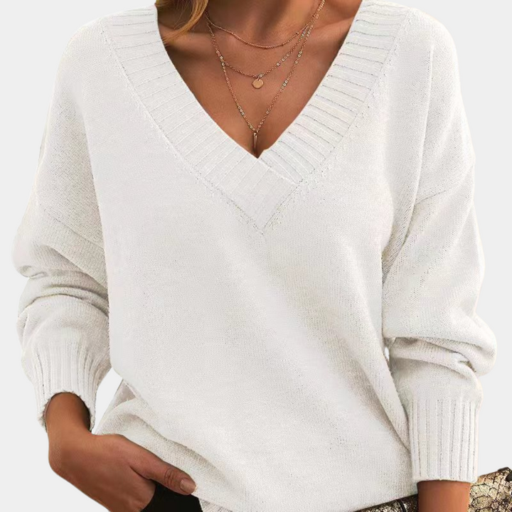 Vrouw draagt witte V-hals trui met lange mouwen en subtiele textuur, gecombineerd met gouden kettingen. Stijlvolle damesmode, herfstkleding.