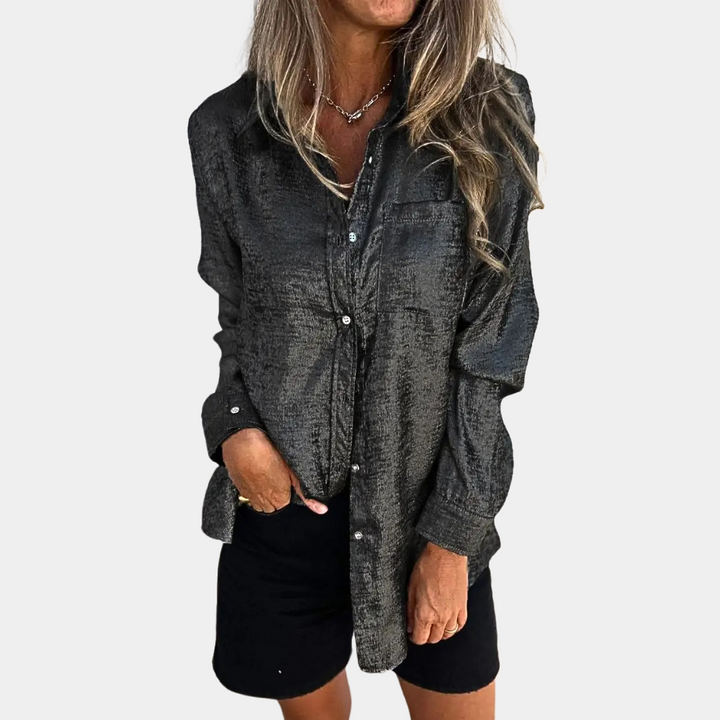 Vrouw draagt zwarte, glanzende blouse met lange mouwen en knopen, gecombineerd met zwarte shorts. Modieuze dameskleding, casual stijl.