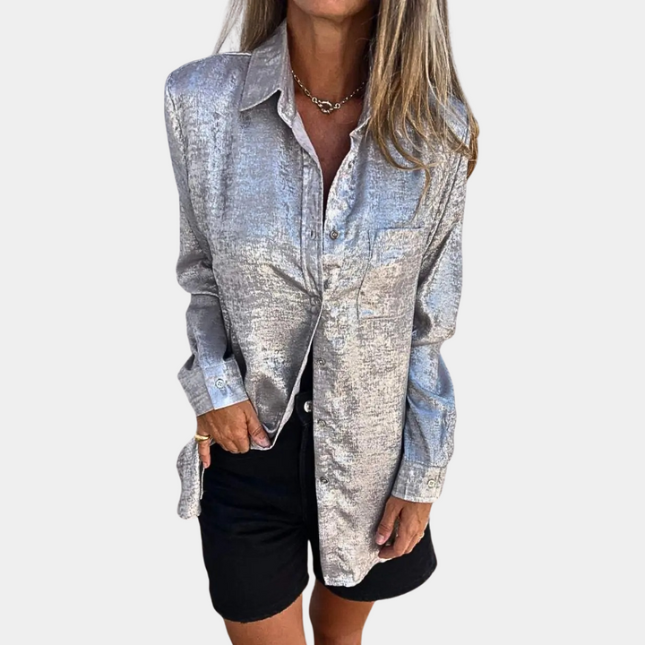 Vrouw draagt zilveren blouse met lange mouwen en zwarte shorts. Modieuze dameskleding, glanzende stof, casual chique look.