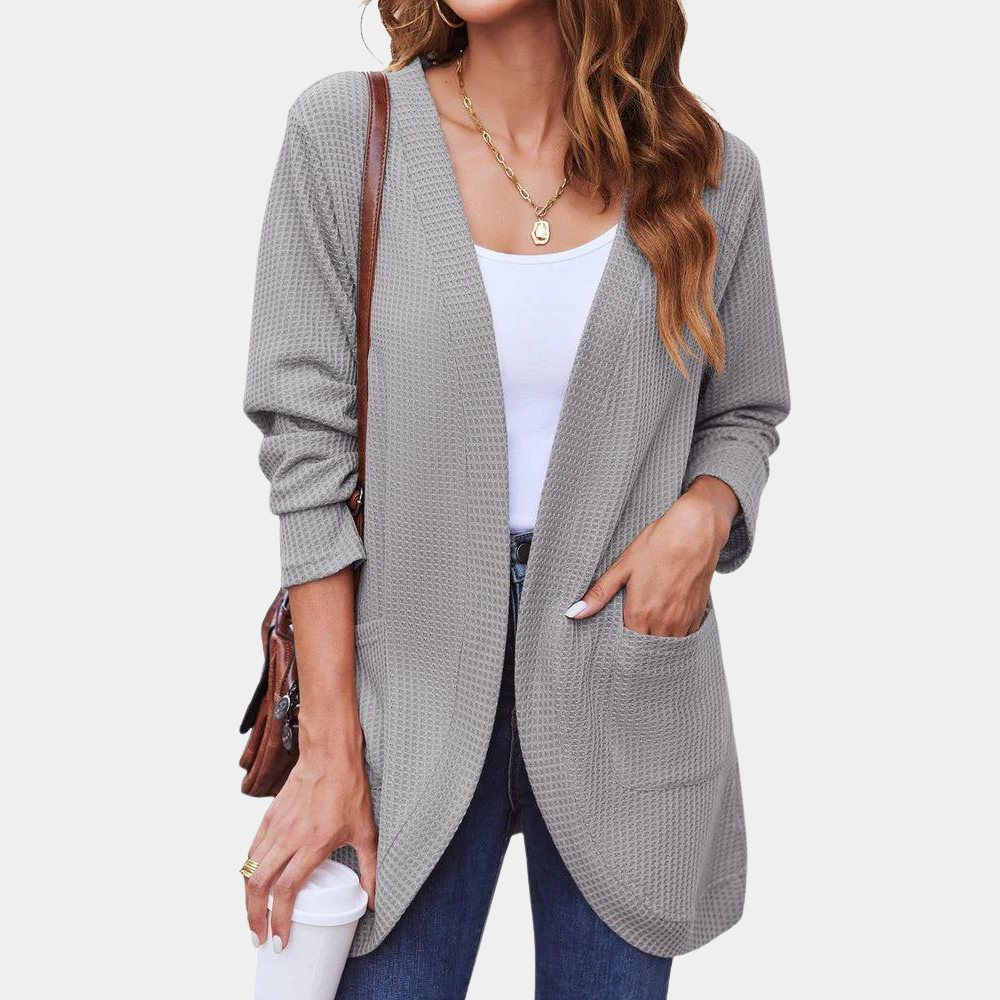 Vrouw draagt lichtgrijs vest met textuur, witte top en jeans. Casual damesmode, herfstkleding, comfortabele stijl, trendy outfit.