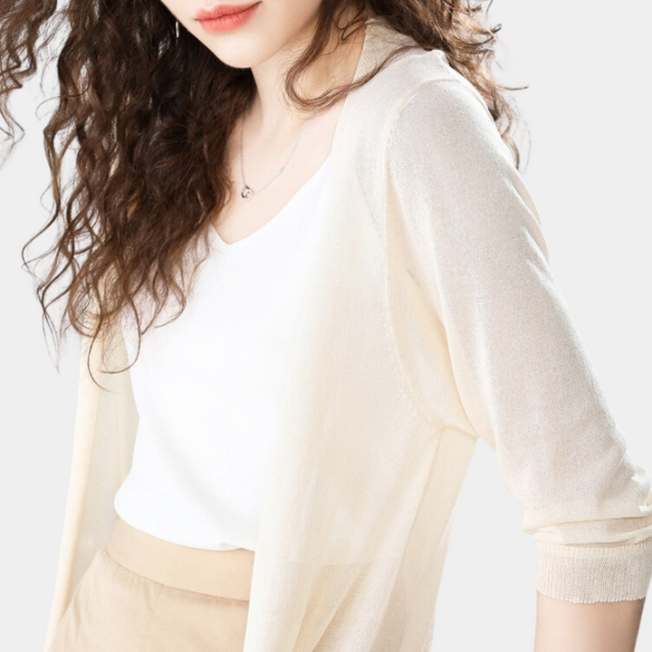 Vrouw in elegante, lichte outfit met witte top en beige vest, modieuze stijl, casual kleding, krullend haar, minimalistische achtergrond.