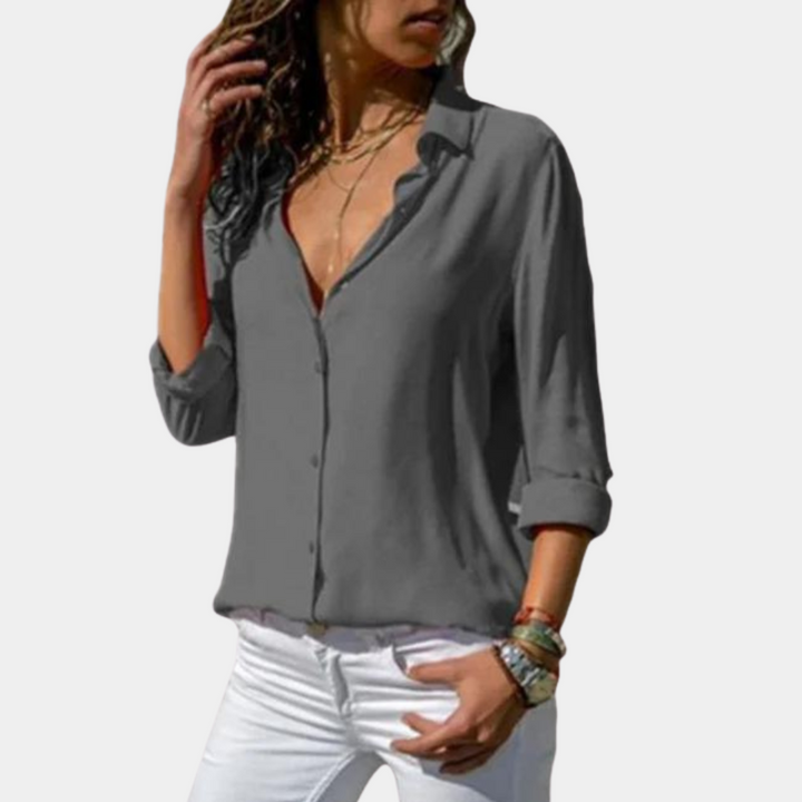 Grijze damesblouse met lange mouwen, V-hals en knoopsluiting, gedragen met witte broek. Modieuze casual outfit voor dames.