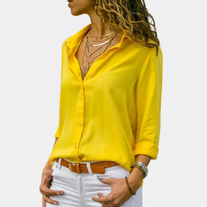 Vrouw in gele blouse met opgerolde mouwen, witte broek en bruine riem. Modieuze dameskleding, casual stijl, trendy outfit.