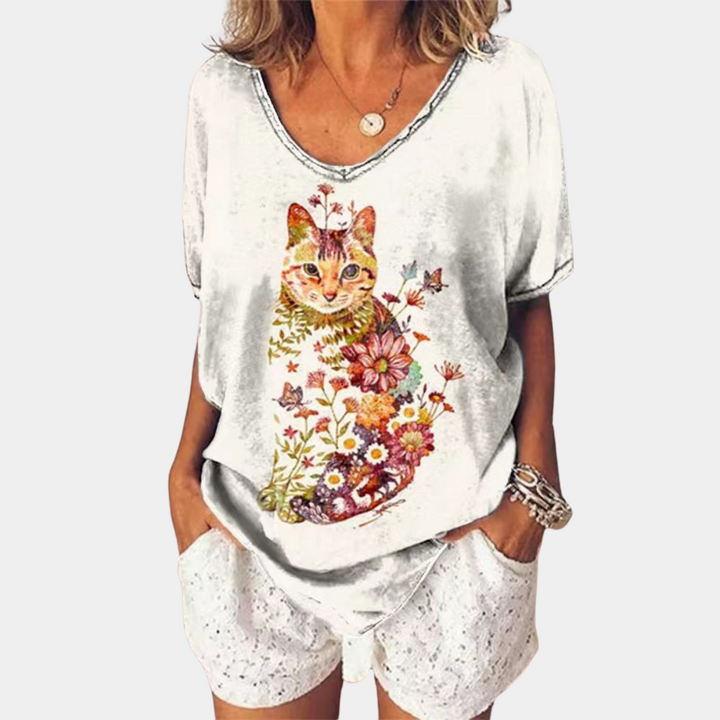 Vrouw draagt wit T-shirt met kleurrijke kattenprint en bloemen, casual zomermode, dameskleding, trendy outfit, comfortabele stijl.