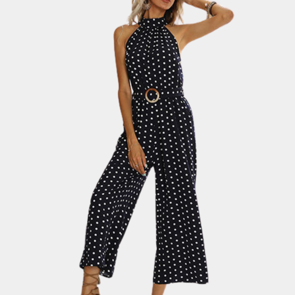 Vrouw in marineblauwe jumpsuit met witte stippen en halternek, modieuze riem, trendy zomeroutfit, casual dameskleding.