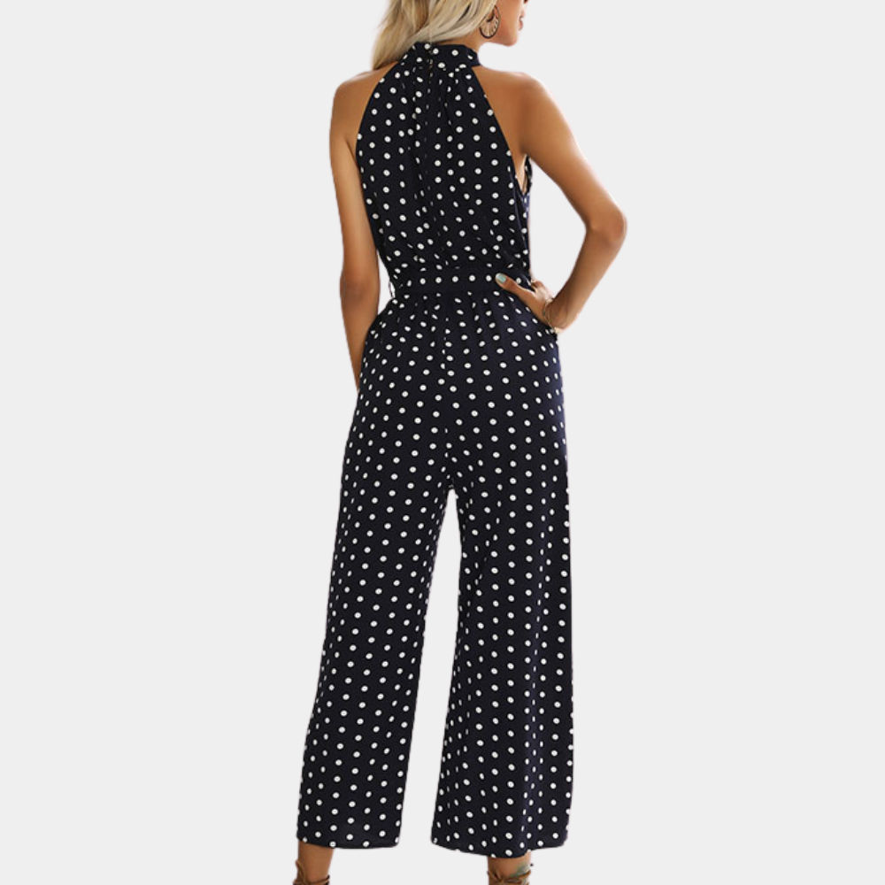Vrouw in marineblauwe jumpsuit met witte stippen, halternek en wijde pijpen. Modieuze dameskleding, trendy zomeroutfit.