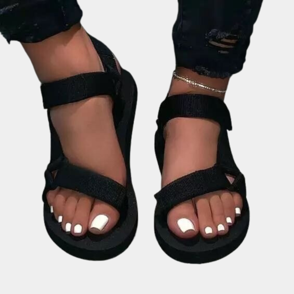 Zwarte sandalen met klittenbandsluiting, gedragen door een persoon met witte gelakte teennagels. Comfortabele zomerschoenen voor dames.