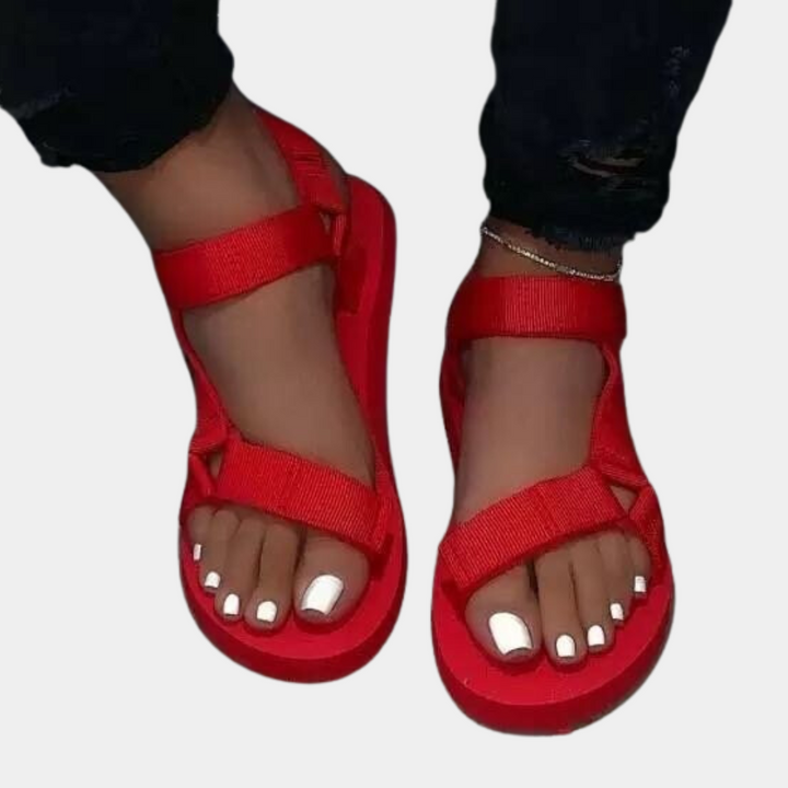 Rode sandalen met klittenbandsluiting, gedragen door een persoon met witte gelakte teennagels. Comfortabele zomerschoenen voor dames.