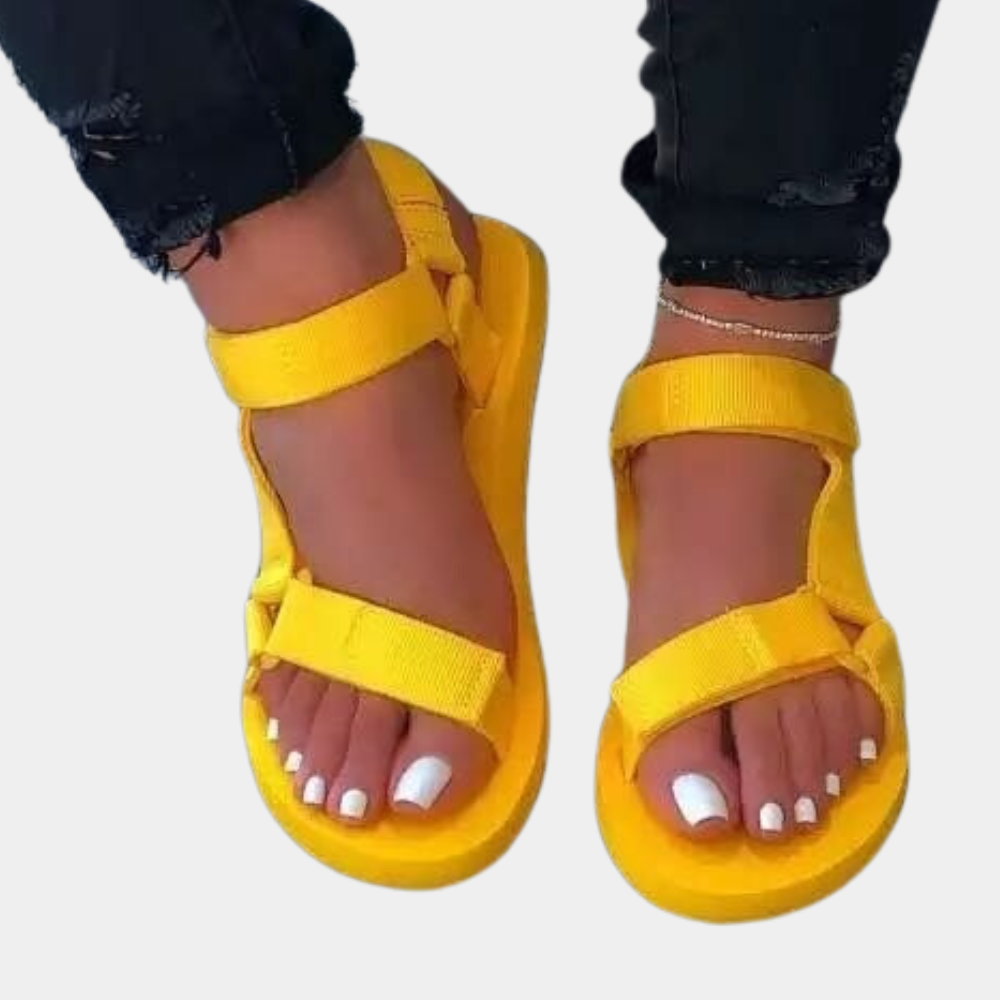 Gele sandalen met klittenband, gedragen door een persoon met witte nagellak. Comfortabele zomerschoenen, perfect voor casual outfits.