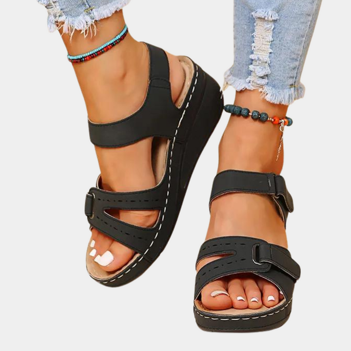 Zwarte sandalen met sleehak, gedragen door een persoon met gescheurde jeans en kleurrijke enkelbandjes. Comfortabele zomerschoenen voor dames.