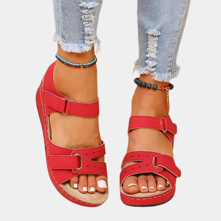 Rode sandalen met klittenband, gedragen met gescheurde jeans en enkelbandjes. Comfortabele zomerschoenen voor dames. Trendy en casual stijl.