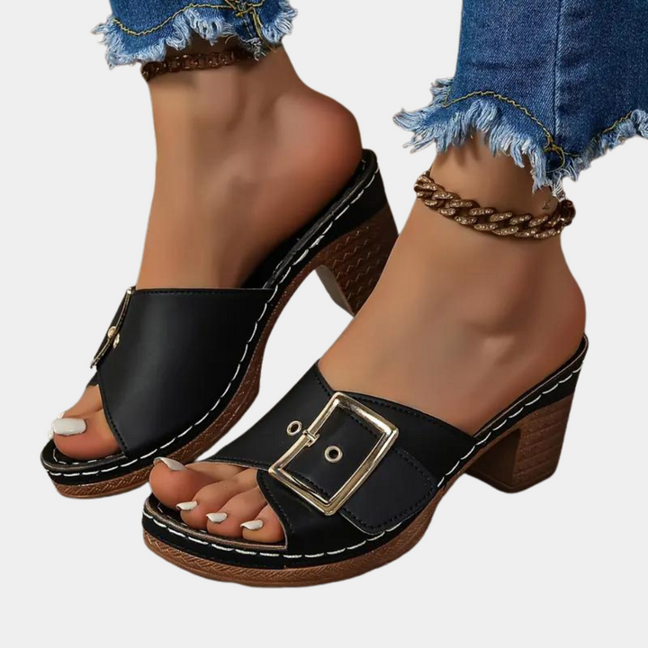Zwarte leren damesmuiltjes met open teen, houten blokhak en grote gesp. Trendy zomerschoenen, perfect voor casual en chique outfits.