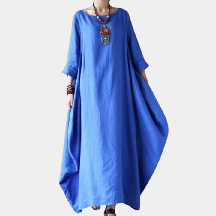 Blauwe maxi-jurk met lange mouwen, losse pasvorm en ronde hals. Ideaal voor casual zomeroutfits. Accessoires: kleurrijke ketting, armbanden.