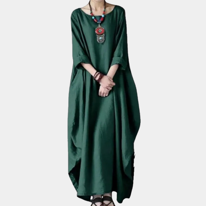 Donkergroene maxi-jurk met lange mouwen, ronde hals en etnische ketting. Boho-stijl dameskleding, comfortabel en elegant ontwerp.