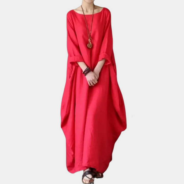 Rode maxi-jurk met lange mouwen, losse pasvorm en ronde hals. Ideaal voor casual zomeroutfits. Vrouw draagt sandalen en houten ketting.