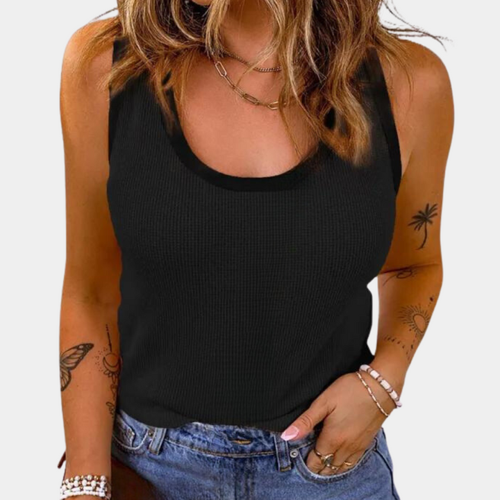 Vrouw in zwarte tanktop, casual outfit met jeans, sieraden en tatoeages. Modieuze zomerkleding, trendy damesmode, casual stijl.