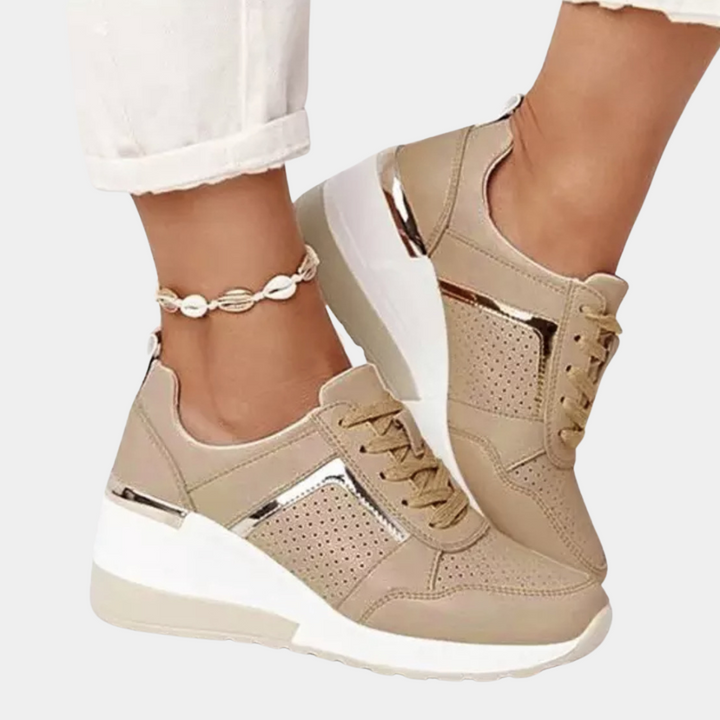 Beige damessneakers met sleehak, metallic details en perforaties, gedragen met witte broek. Trendy schoenen voor casual en sportieve outfits.