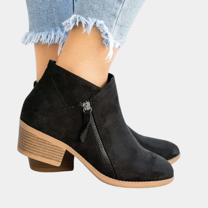 Zwarte suède enkellaarsjes met rits en blokhak, gedragen met lichtblauwe gerafelde jeans. Stijlvolle damesmode, comfortabele herfstschoenen.