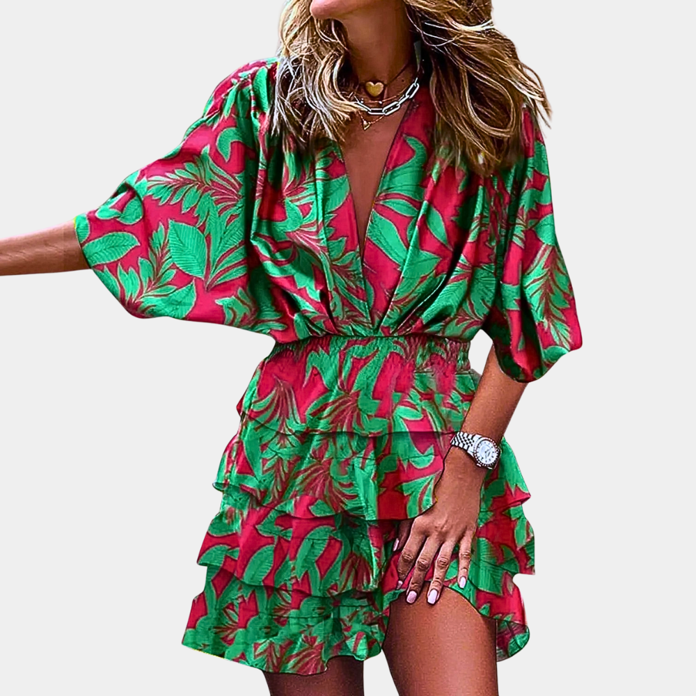 Vrouw in kleurrijke zomerjurk met groene en rode bladerenprint, korte mouwen en V-hals. Perfect voor casual en strandmode.