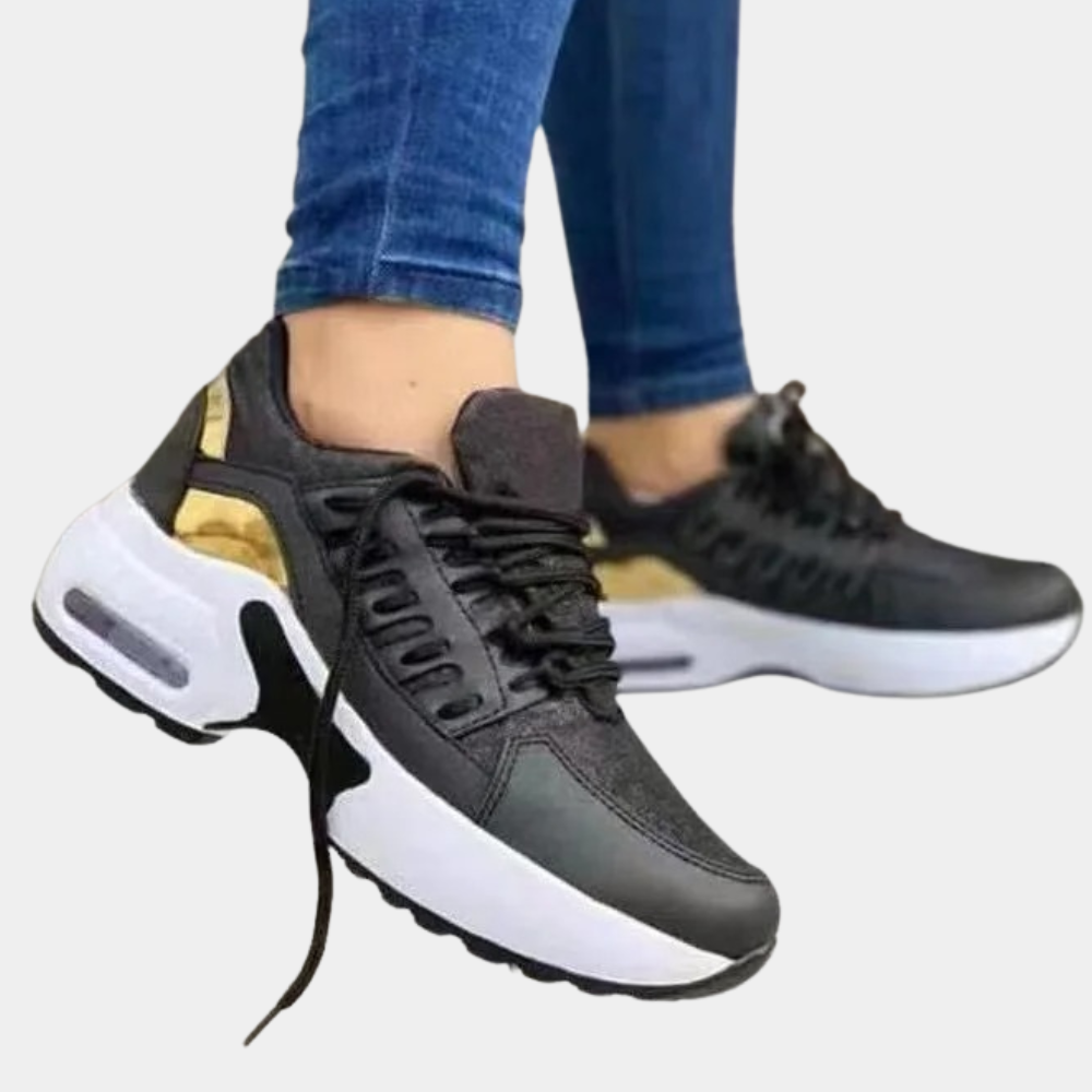 Zwarte sneakers met witte zool en gouden details, gedragen door persoon in blauwe jeans. Modieuze sportschoenen, comfortabel en trendy design.