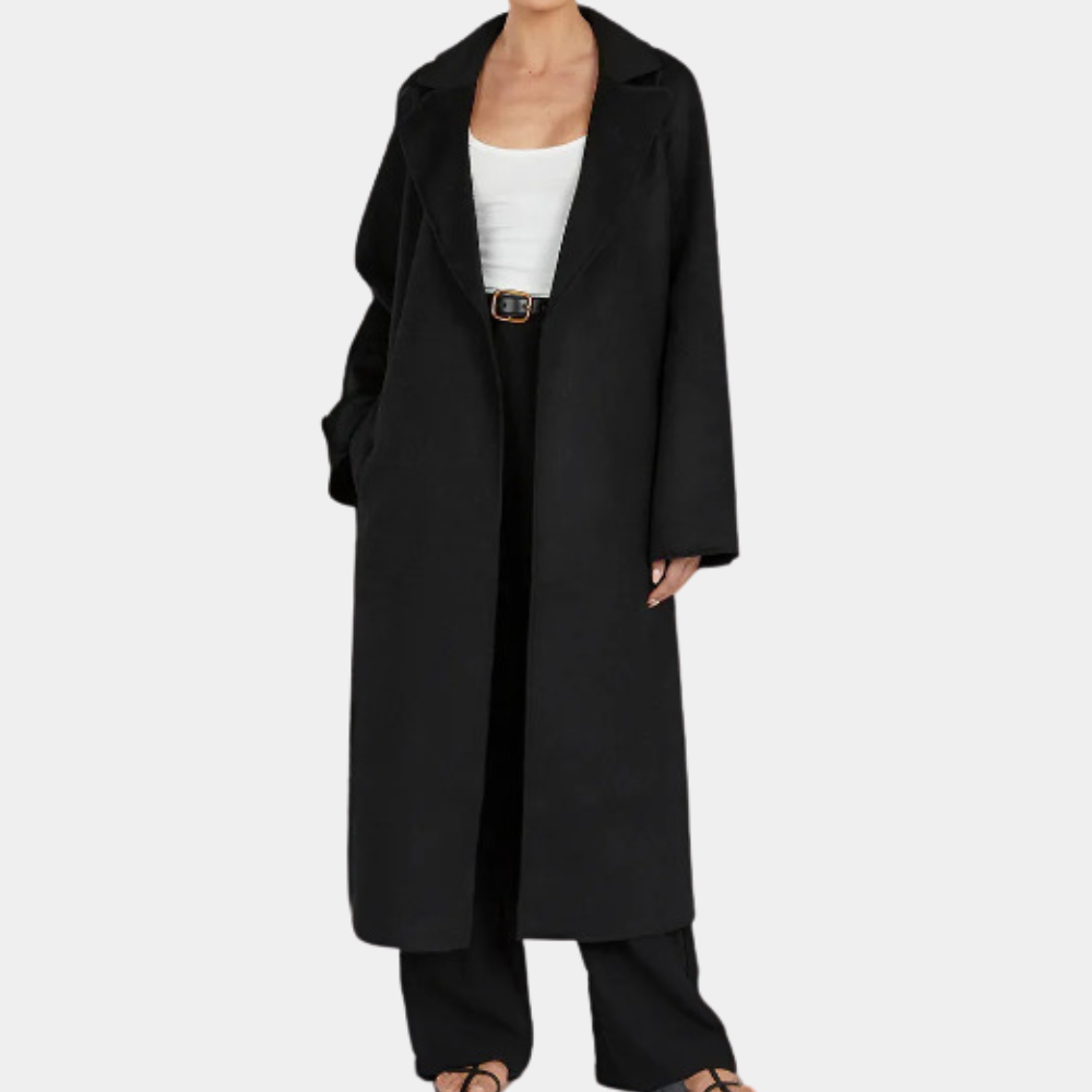Zwarte lange damesjas, open gedragen over witte top en zwarte broek, modieuze herfst- en winterkleding, minimalistisch design.