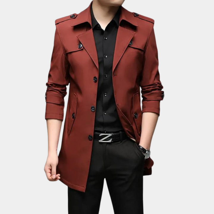 Wijnrode herenjas met knopen, epauletten en opstaande kraag, gedragen over een zwarte blouse en broek. Stijlvolle herenkleding voor herfstmode.