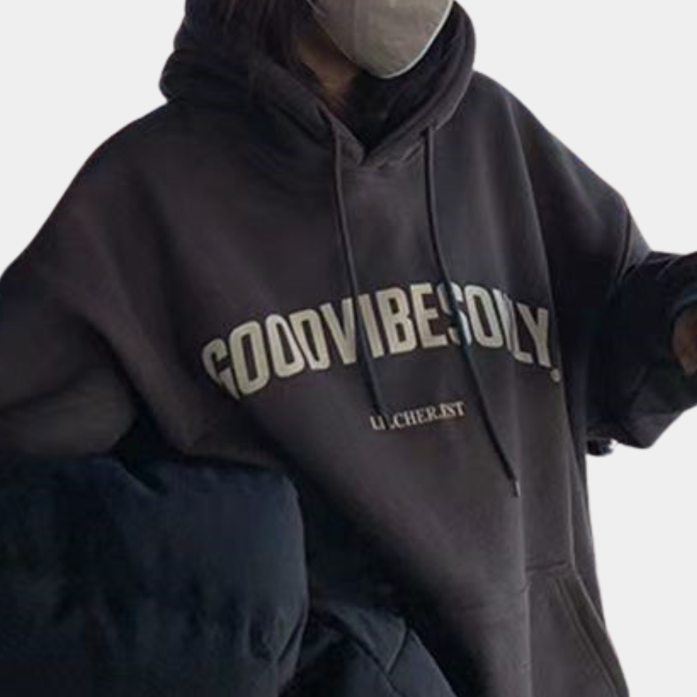 Grijze hoodie met "GOOD VIBES ONLY" opdruk, gedragen door persoon met mondkapje. Comfortabele streetwear, casual mode, unisex kledingstijl.