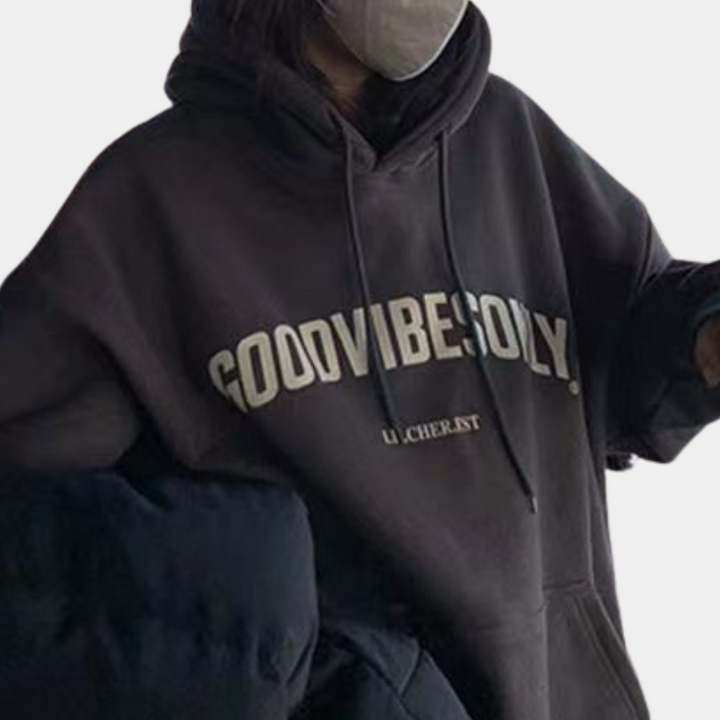 Grijze hoodie met "GOOD VIBES ONLY" opdruk, gedragen door persoon met mondkapje. Comfortabele streetwear, casual mode, unisex kledingstijl.