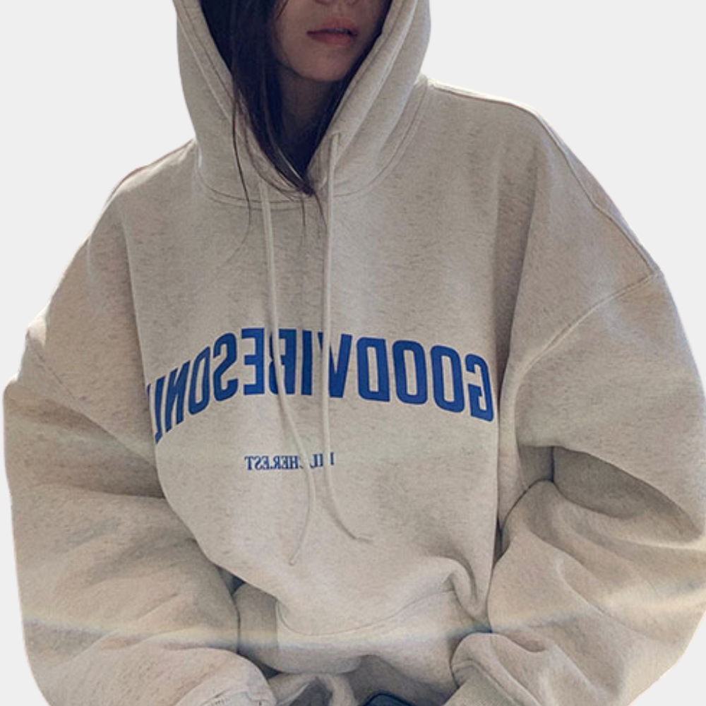 Vrouw in oversized witte hoodie met blauwe tekst "GOODVIBESONLY". Comfortabele streetwear, casual mode, trendy kledingstijl.