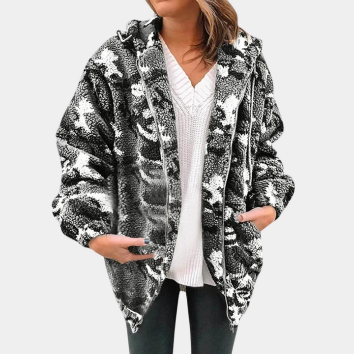 Vrouw draagt oversized zwart-witte camouflage fleecejas met capuchon, gecombineerd met witte trui en zwarte broek. Wintermode, comfortabele stijl.