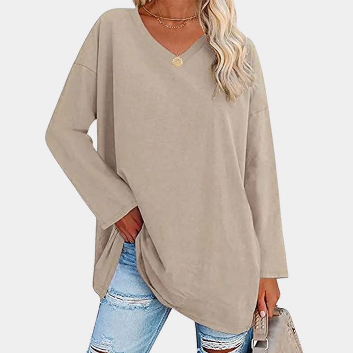 Vrouw in beige oversized trui met V-hals, gecombineerd met gescheurde jeans. Modieuze casual outfit, ideaal voor herfst- en winterseizoenen.