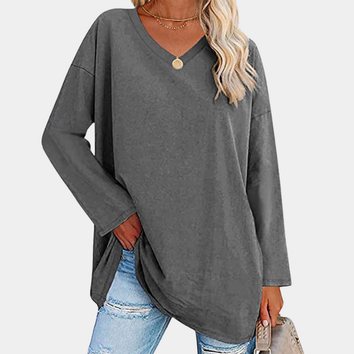 Vrouw draagt donkergrijze oversized trui met V-hals, gecombineerd met gescheurde jeans. Modieuze casual dameskleding, comfortabele herfstoutfit.
