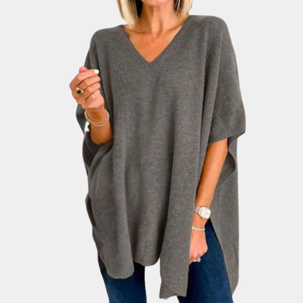 Grijze oversized damestrui met V-hals, gedragen door model. Comfortabele, casual stijl. Perfect voor herfst- en wintermode.