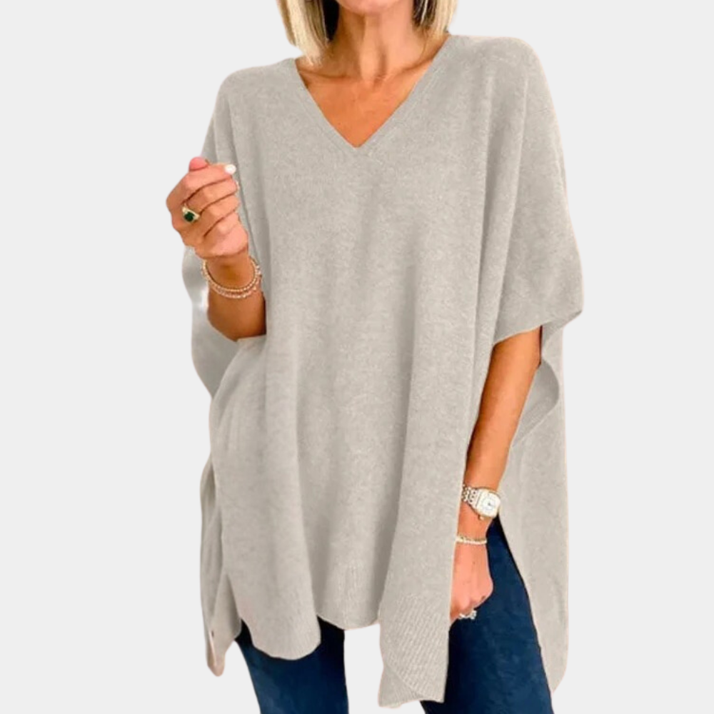 Grijze oversized poncho trui met V-hals, gedragen door vrouw. Modieuze dameskleding, comfortabel en stijlvol voor herfst en winter.