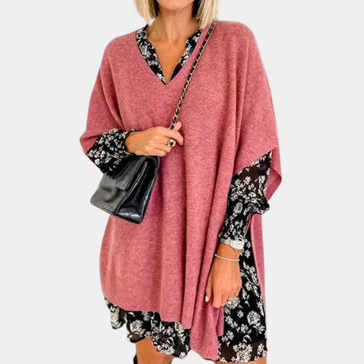 Vrouw in roze poncho met zwarte bloemenjurk en zwarte schoudertas. Modieuze herfstoutfit, trendy dameskleding, casual stijl.