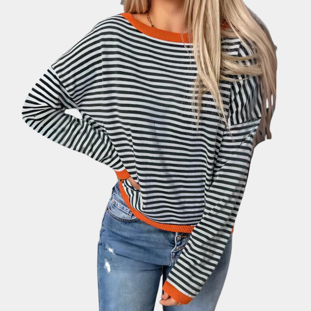 Gestreepte zwart-witte trui met oranje accenten, gedragen door vrouw met blond haar, gecombineerd met blauwe jeans. Modieuze dameskleding.