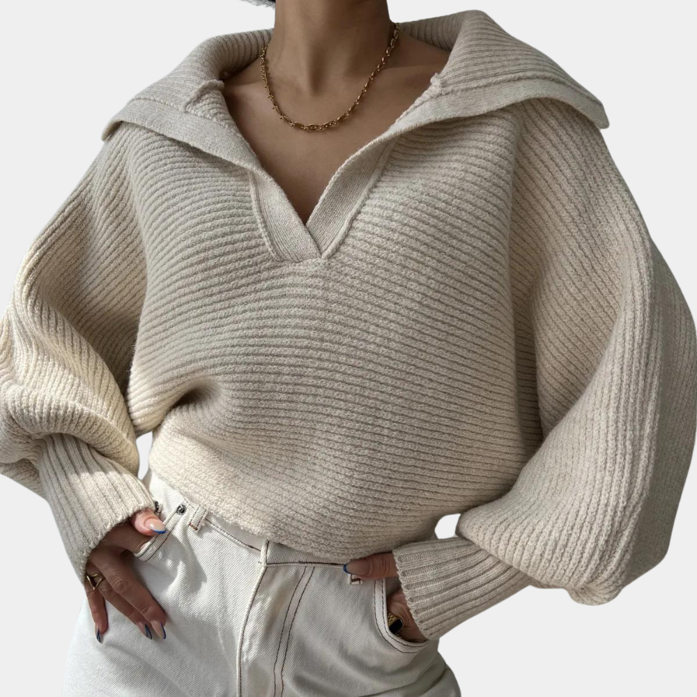 Vrouw draagt een crèmekleurige, geribbelde trui met kraag en wijde mouwen, gecombineerd met witte jeans. Modieuze dameskleding, herfststijl.