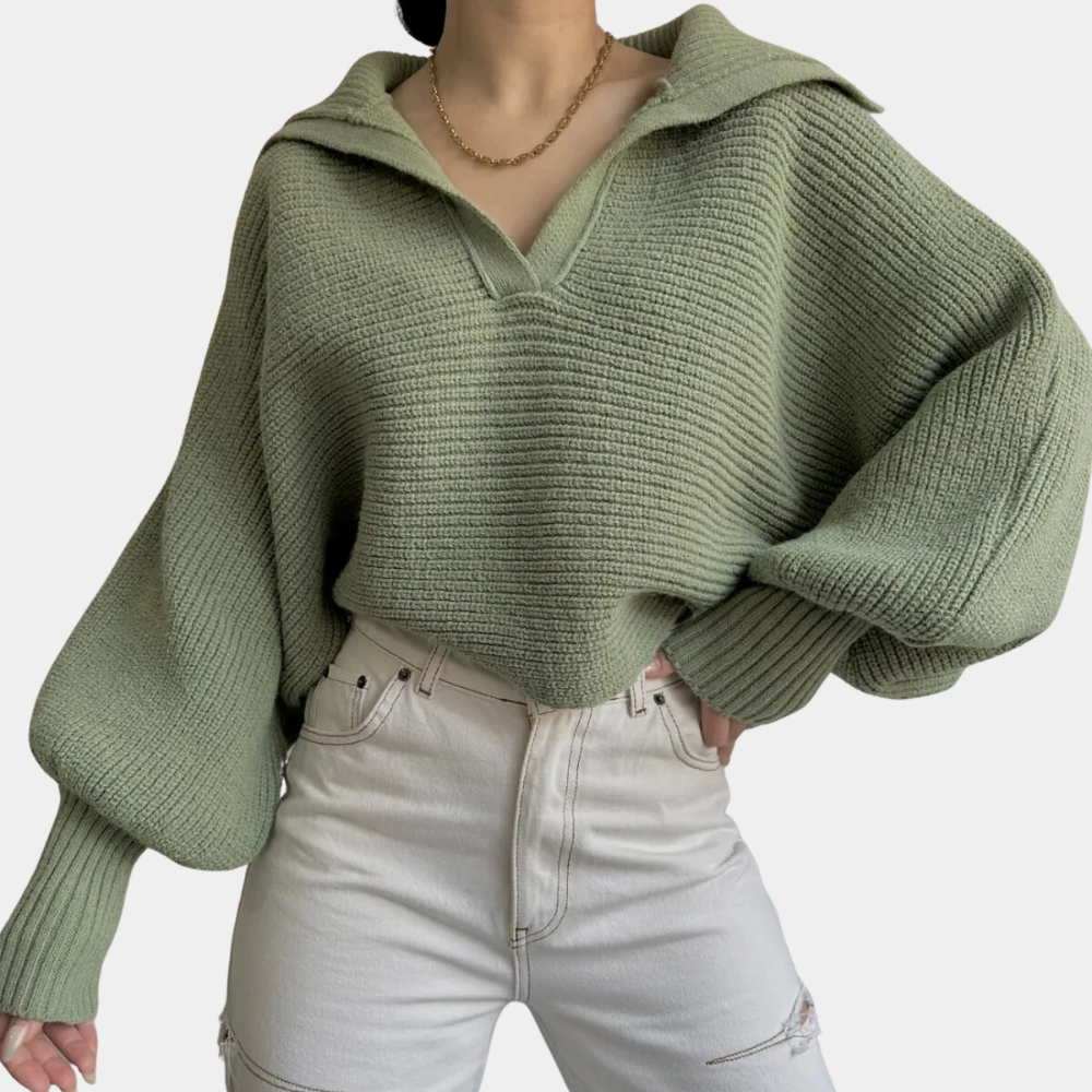 Vrouw draagt een oversized groene gebreide trui met kraag en wijde mouwen, gecombineerd met witte high-waisted jeans. Modieuze herfstoutfit.