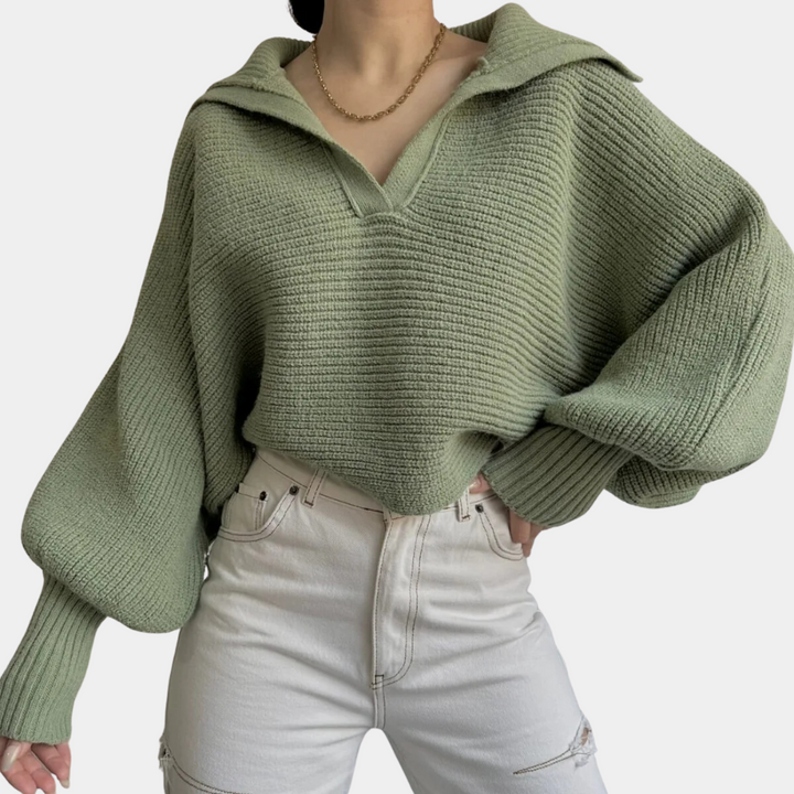 Vrouw draagt een oversized groene gebreide trui met kraag en wijde mouwen, gecombineerd met witte high-waisted jeans. Modieuze herfstoutfit.