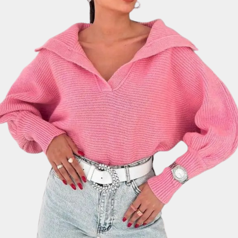 Vrouw draagt roze gebreide trui met wijde mouwen, gecombineerd met lichtblauwe jeans en witte riem. Modieuze dameskleding, casual stijl.