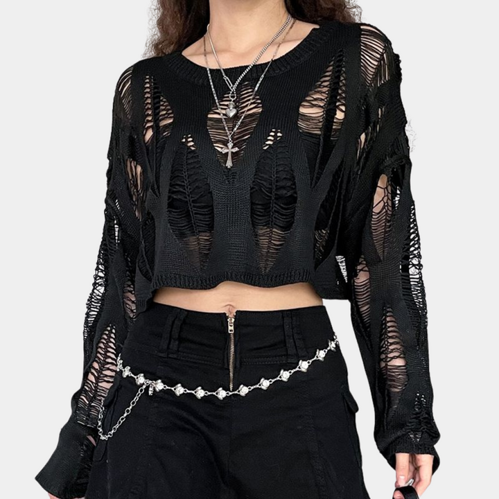 Vrouw in zwarte, gescheurde trui met lange mouwen en kettingriem. Modieuze streetwear, edgy stijl, trendy kleding voor dames.
