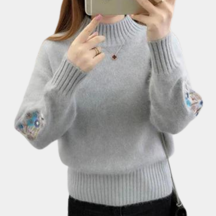 Grijze damestrui met geborduurde elleboogpatches, lange mouwen en hoge hals. Modieuze winterkleding, comfortabel en stijlvol design.