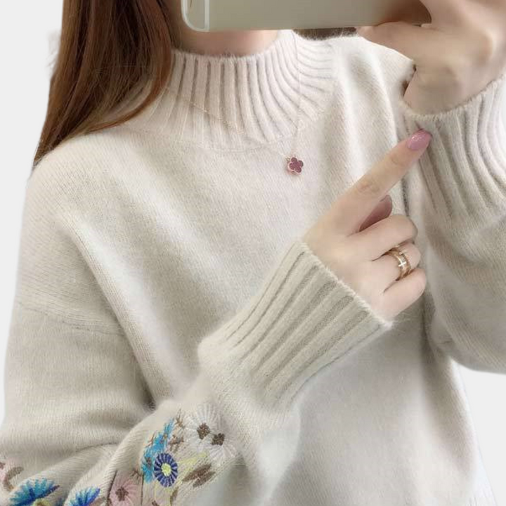 Vrouw draagt crèmekleurige trui met geborduurde bloemen en geribbelde kraag, houdt smartphone vast. Modieuze dameskleding, herfststijl.