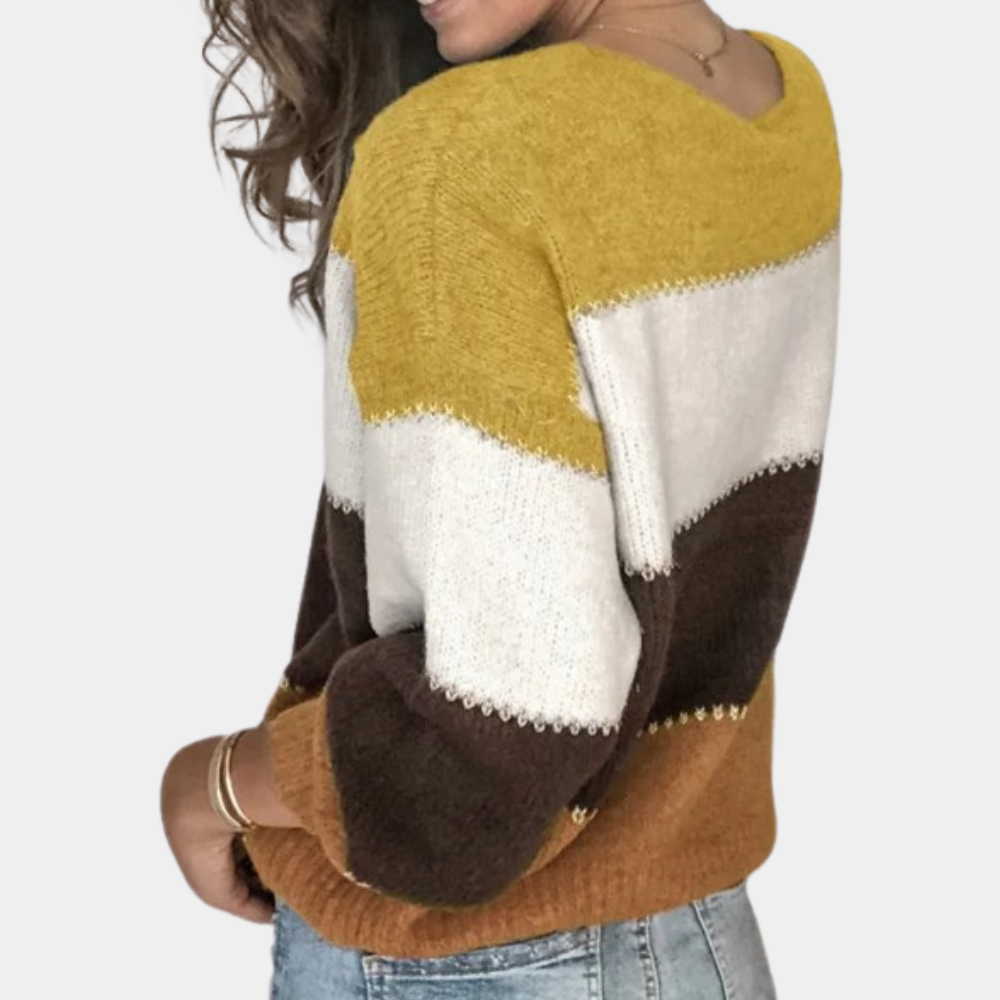Vrouw draagt gebreide trui met kleurblokken in geel, wit, bruin en oranje, gecombineerd met blauwe jeans. Modieuze herfstkleding, casual stijl.